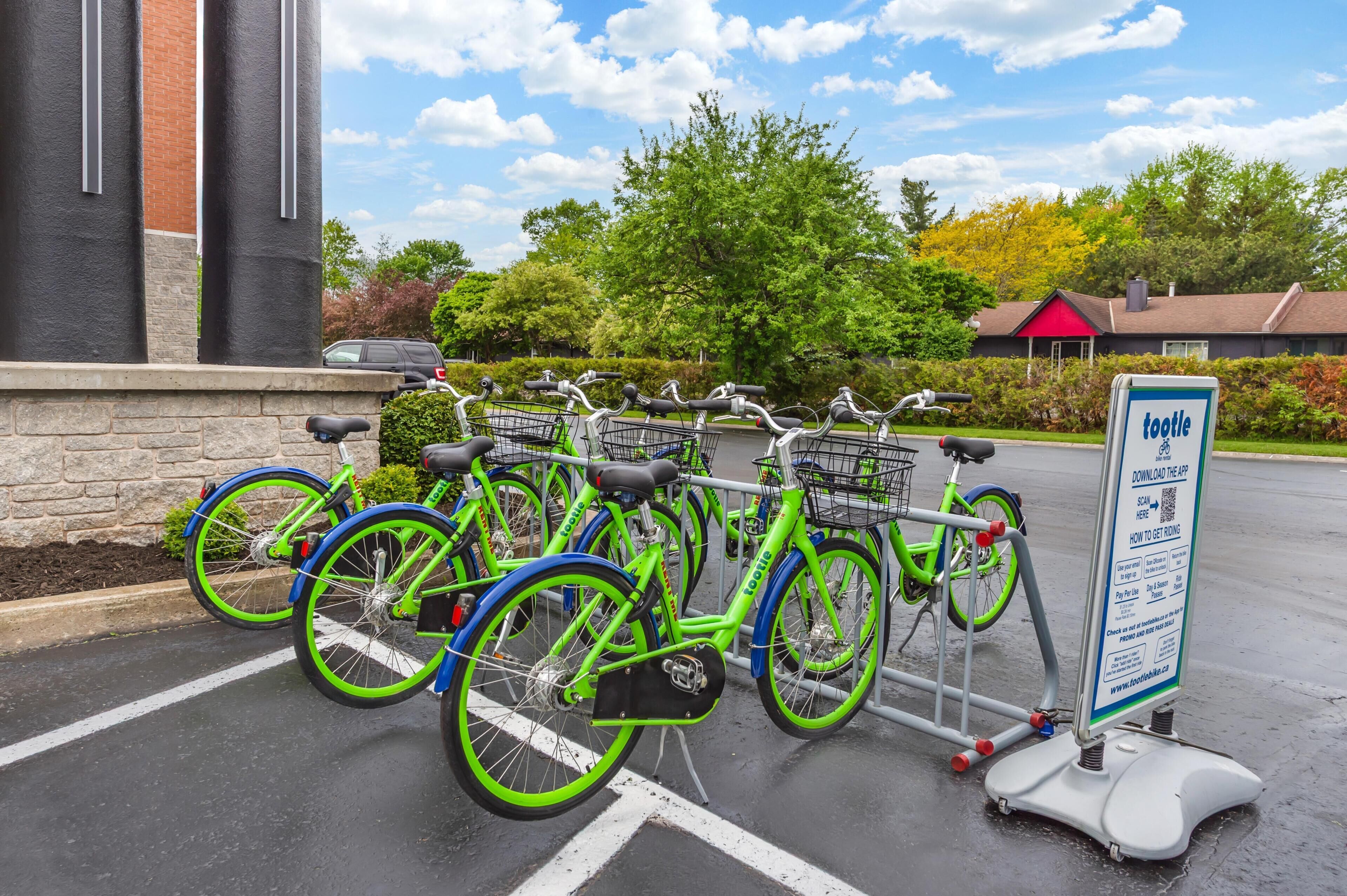 A bicycle rental station with multiple bikes, a QR code sign, and a building with a red roof in the background.