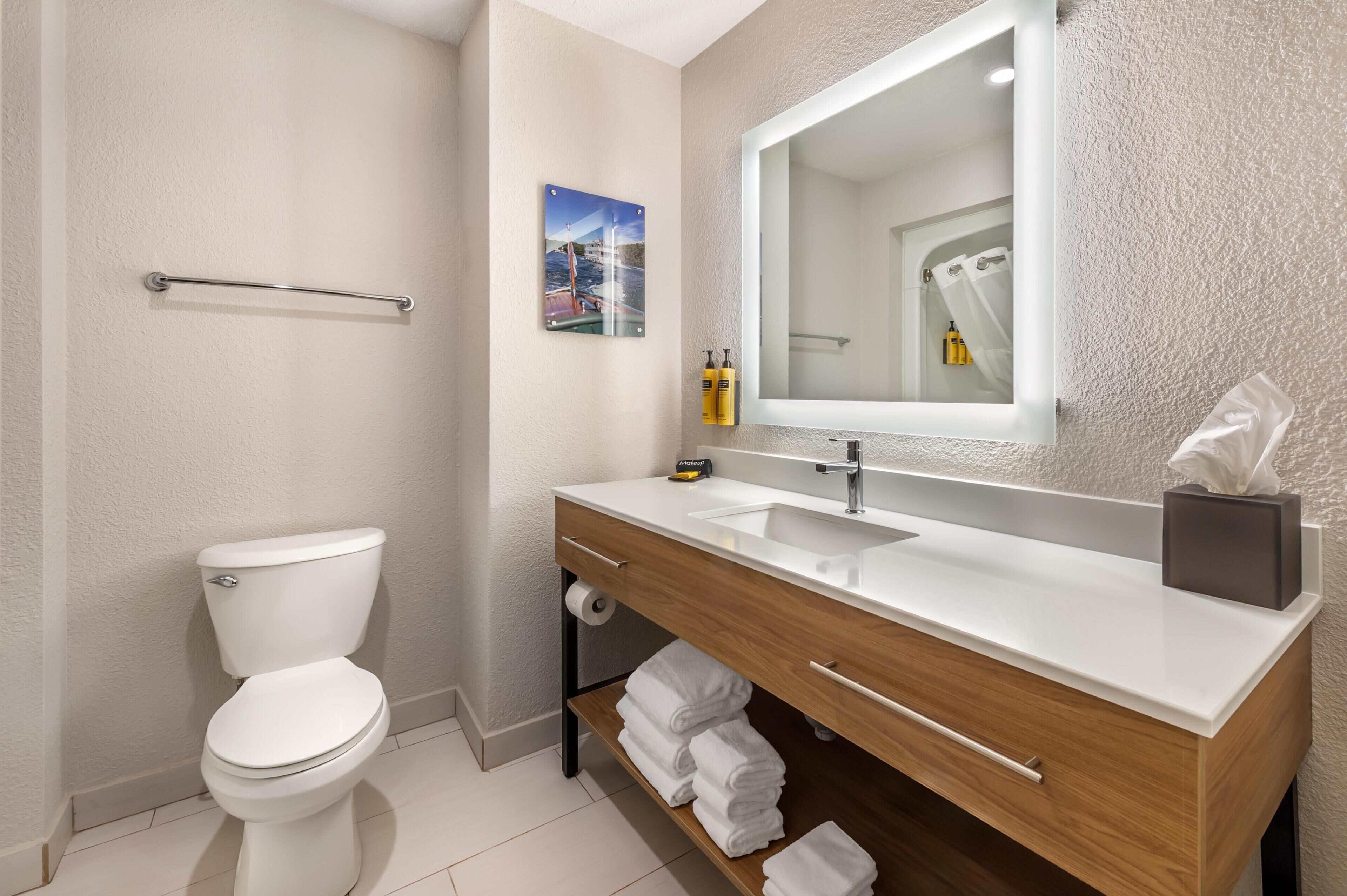 Un baño moderno con inodoro blanco, tocador de madera con lavamanos y un espejo grande.