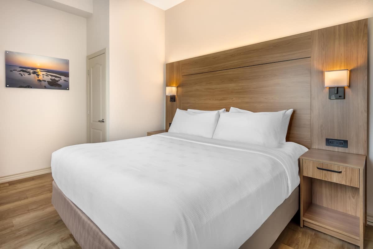 A hotel room with a large bed, wooden headboard, bedside lamps, and a painting on the wall.