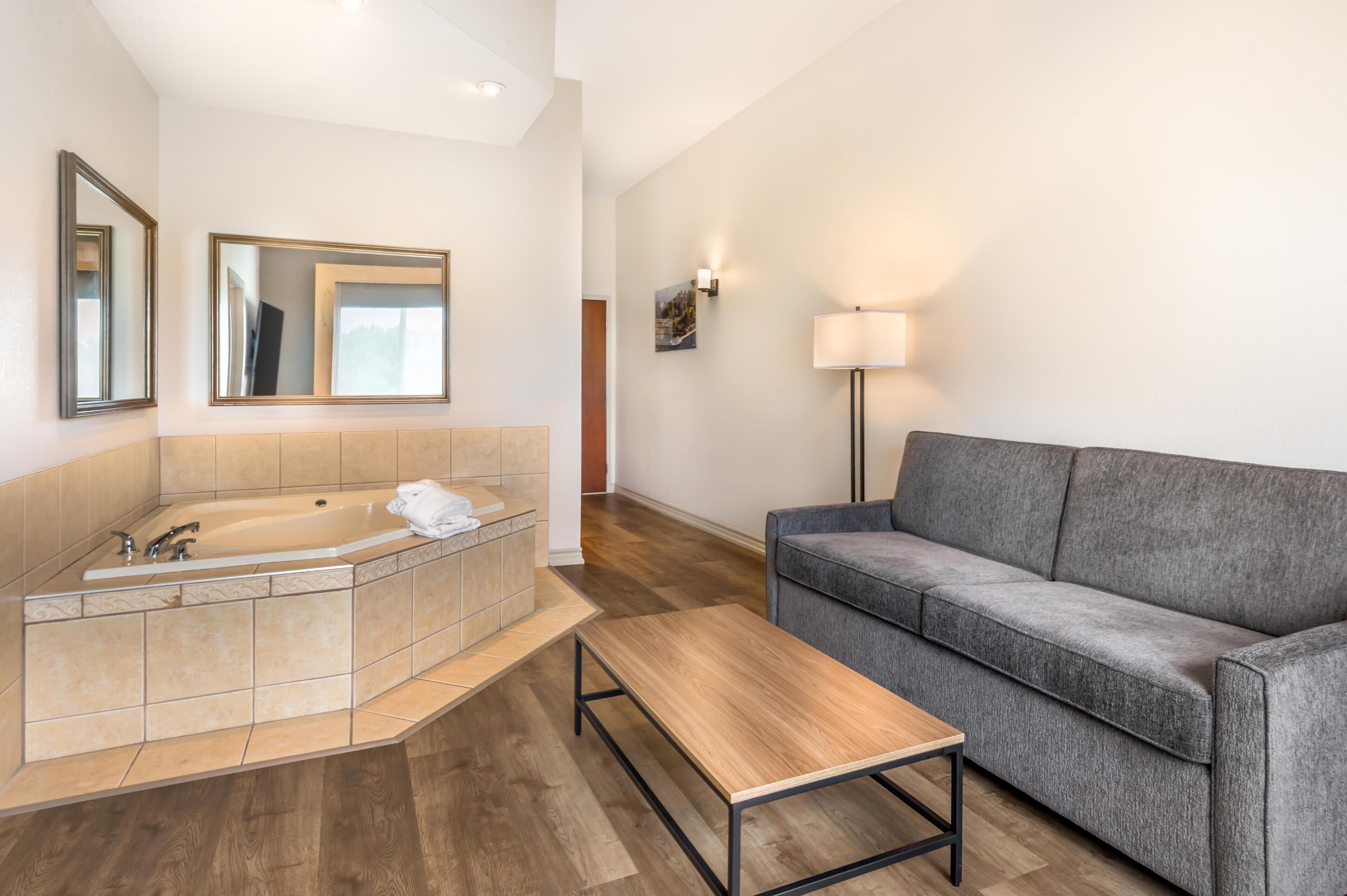 A modern bathroom with a bathtub, a gray sofa, and a wooden table.