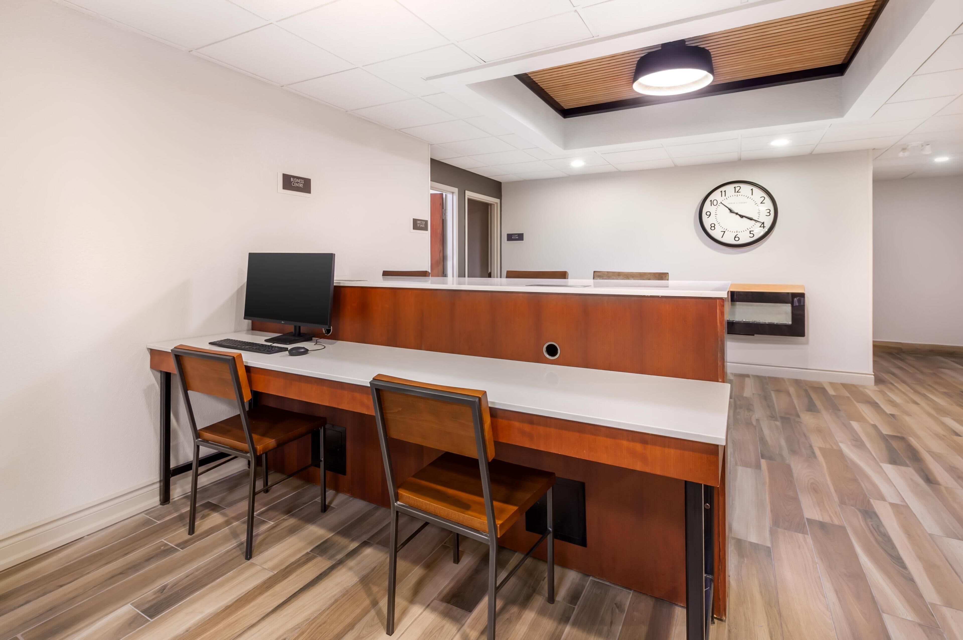 A modern office space with a long desk, chairs, a computer, a clock, and a wooden ceiling.
