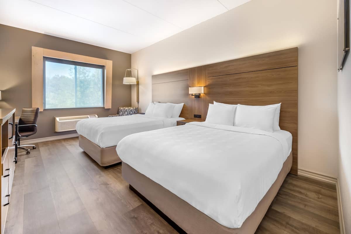 A hotel room with two beds, a desk, a chair, and a large window.