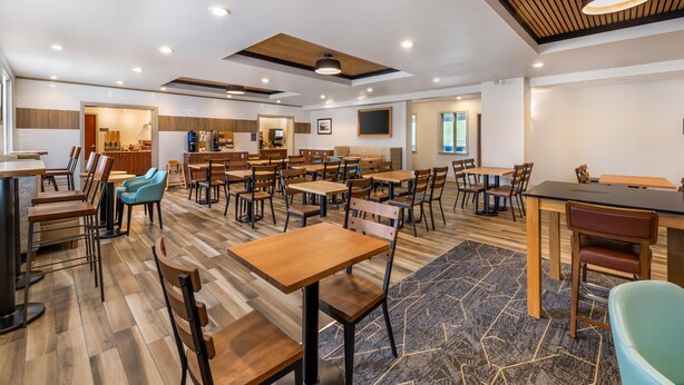 Un grand espace à manger avec plusieurs tables et chaises, une cuisine à l’arrière-plan et un design moderne au niveau du plafond.