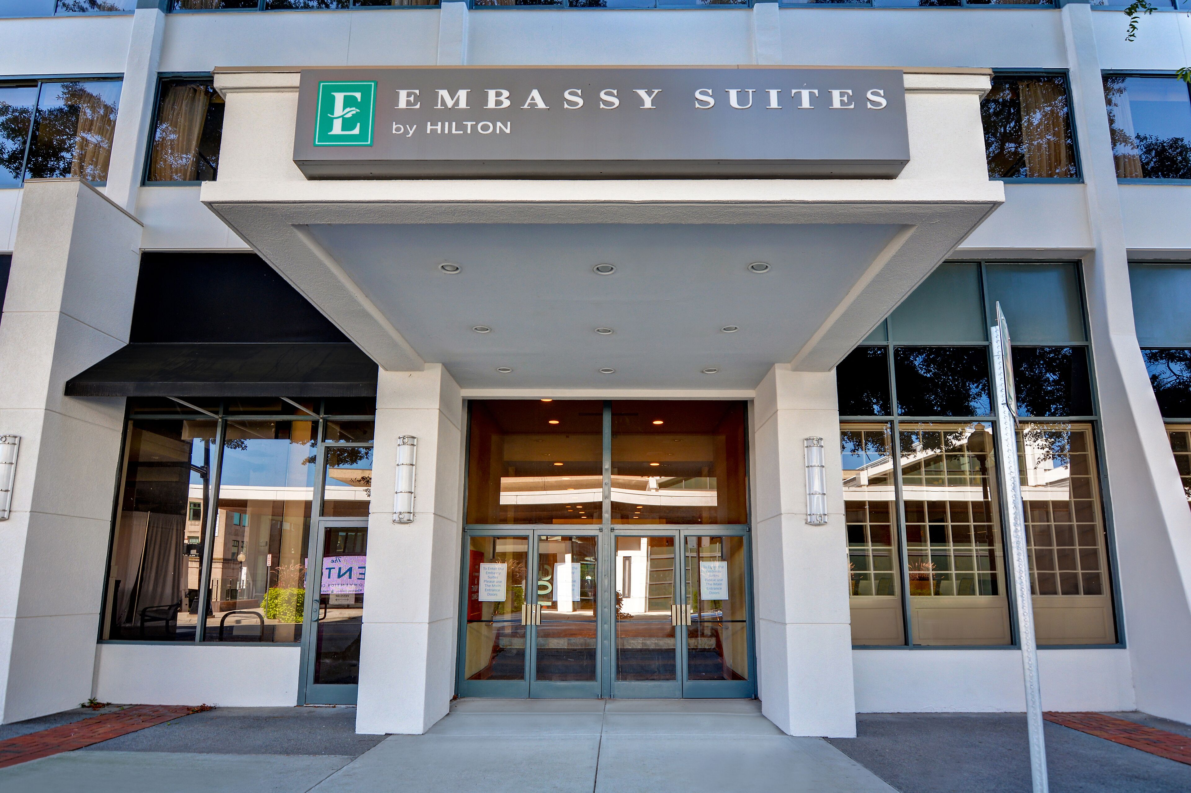 The entrance to Embassy Suites by Hilton with a modern design, large glass doors, and a clear view of the interior through the windows.