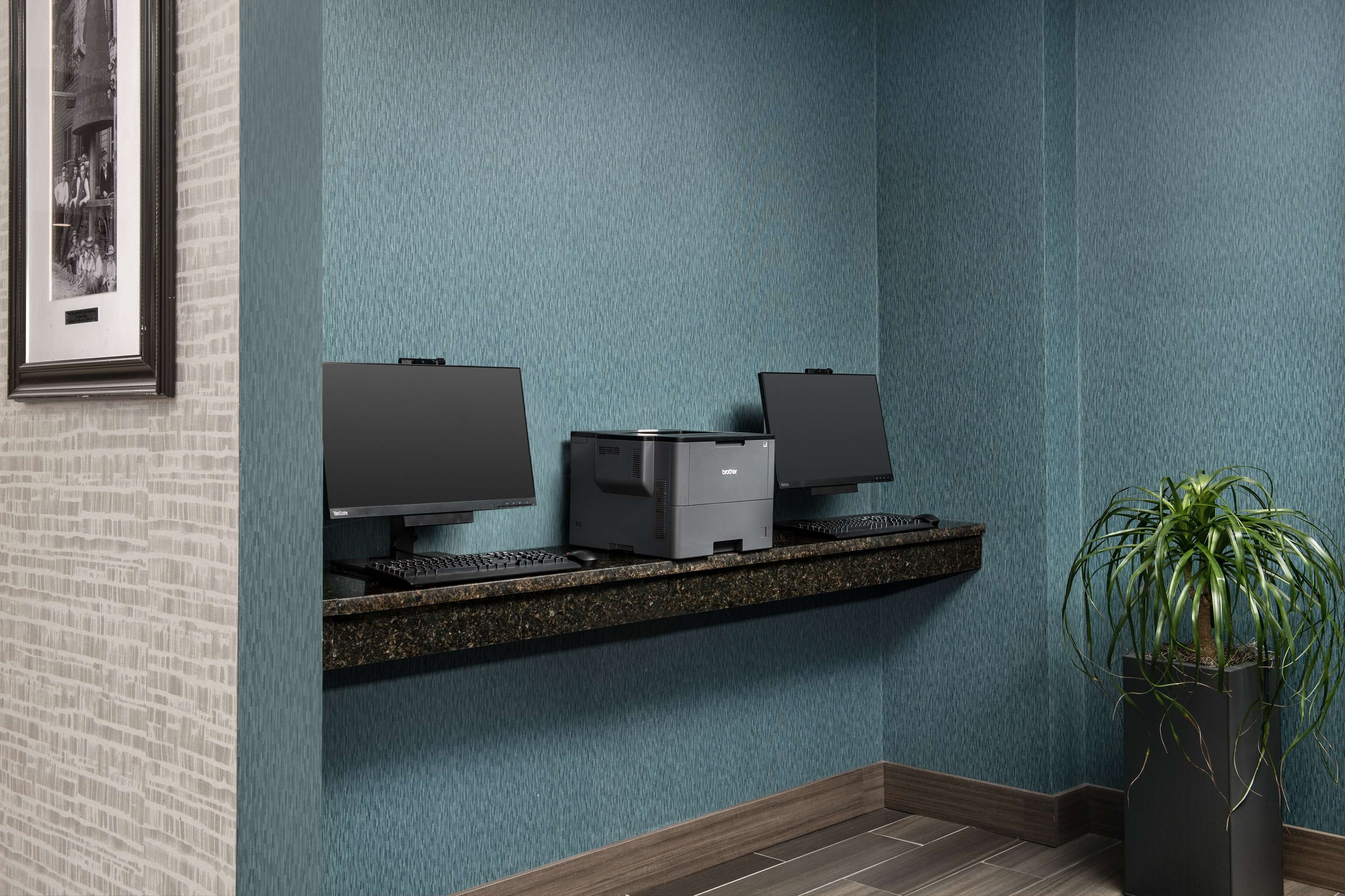 A reception area with a printer, two monitors, a keyboard, and a potted plant.
