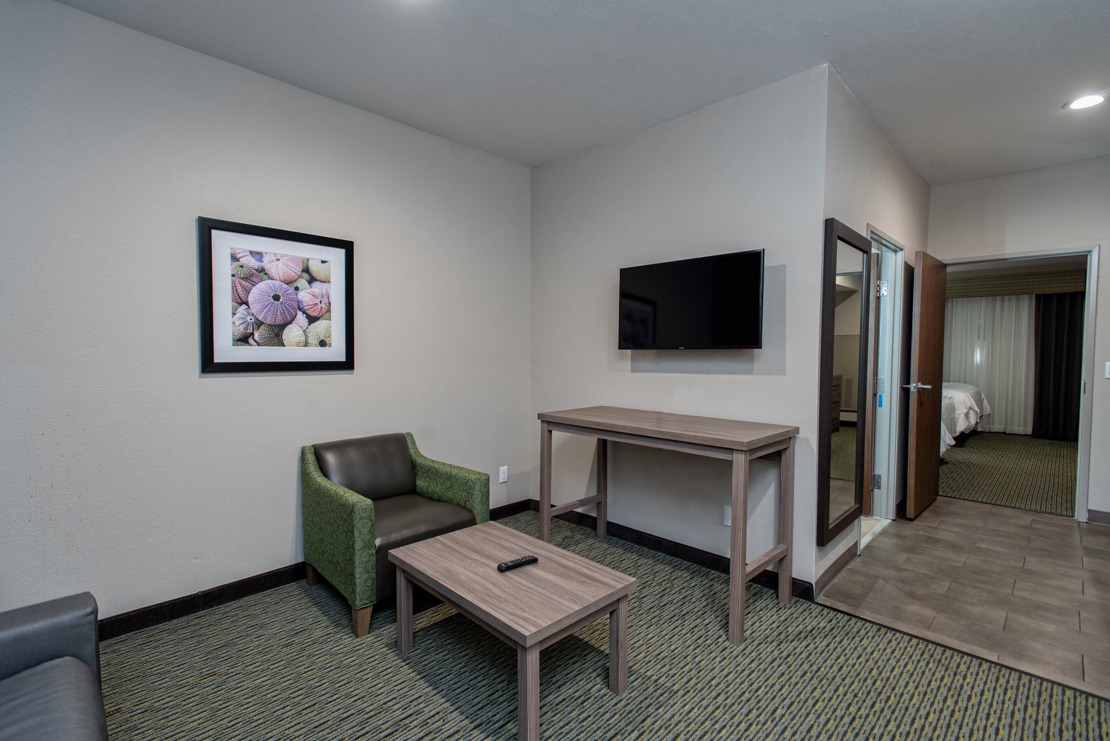 Ein Hotelzimmer mit grünem Sessel, einem kleinen Tisch, einem an der Wand befestigten Fernseher und einem Bett mit Vorhang.