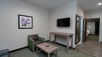 A hotel room with a green armchair, a small table, a TV mounted on the wall, and a bed with a curtain.