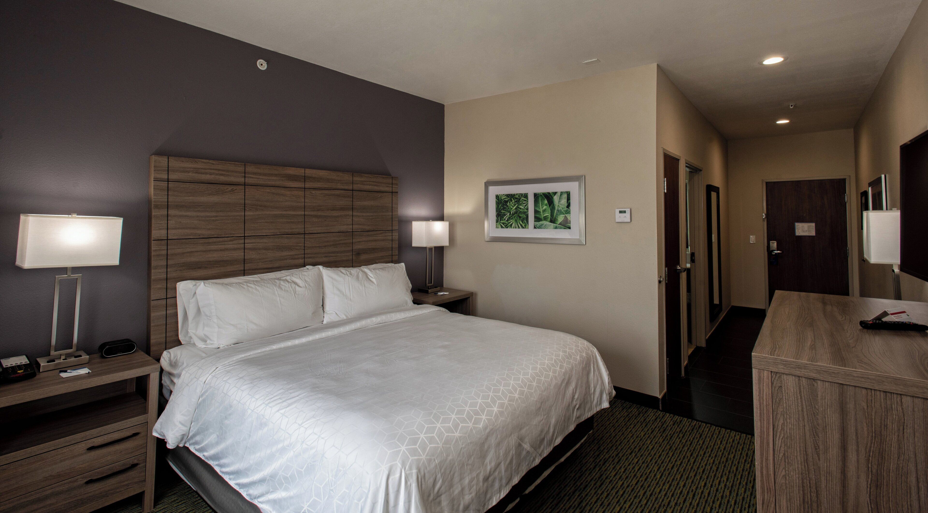 A hotel room with a bed, bedside tables, a desk, a lamp, and a framed picture on the wall.