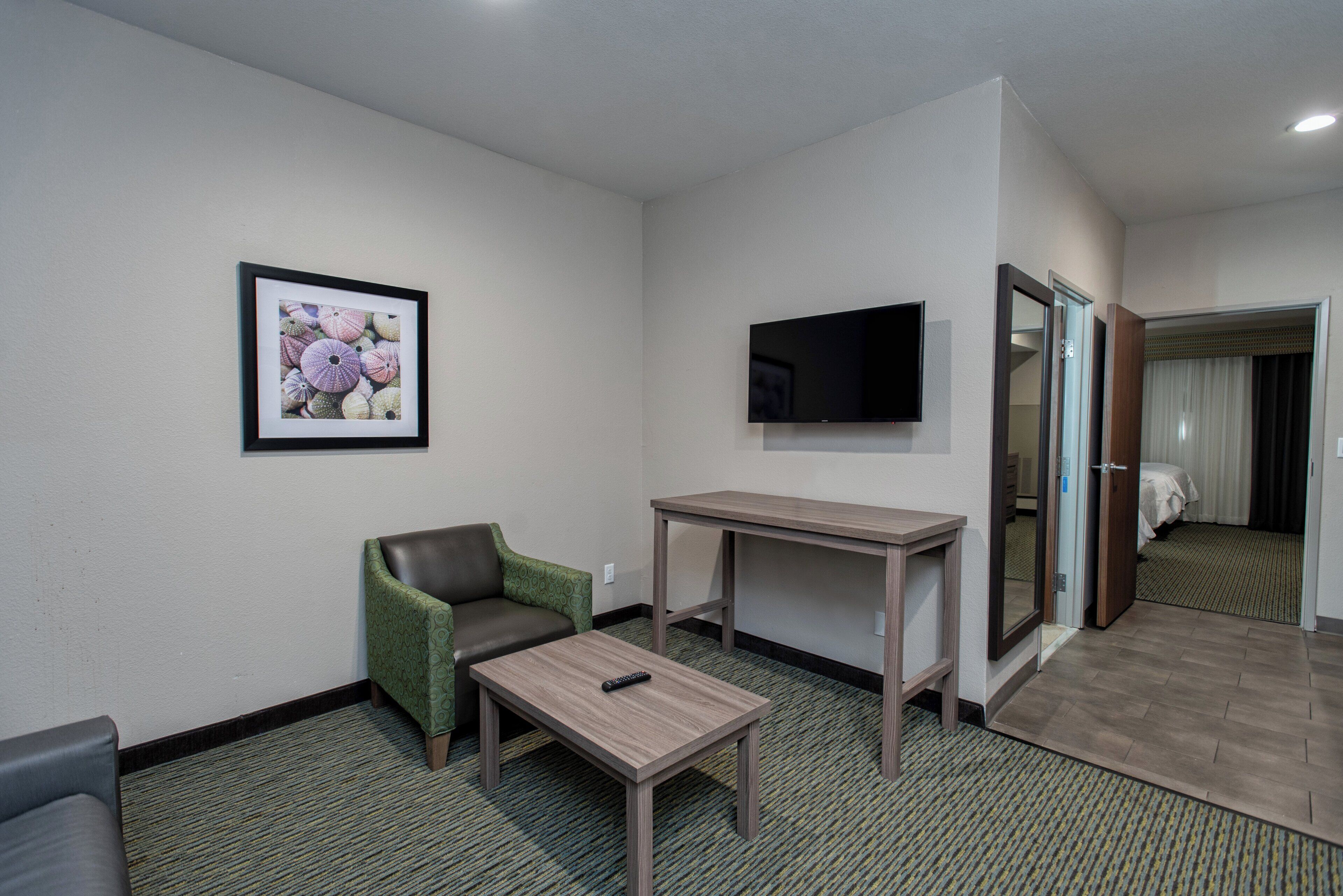 Une chambre d’hôtel avec un fauteuil vert, une petite table, un téléviseur à écran plat et un lit doté d’un rideau.