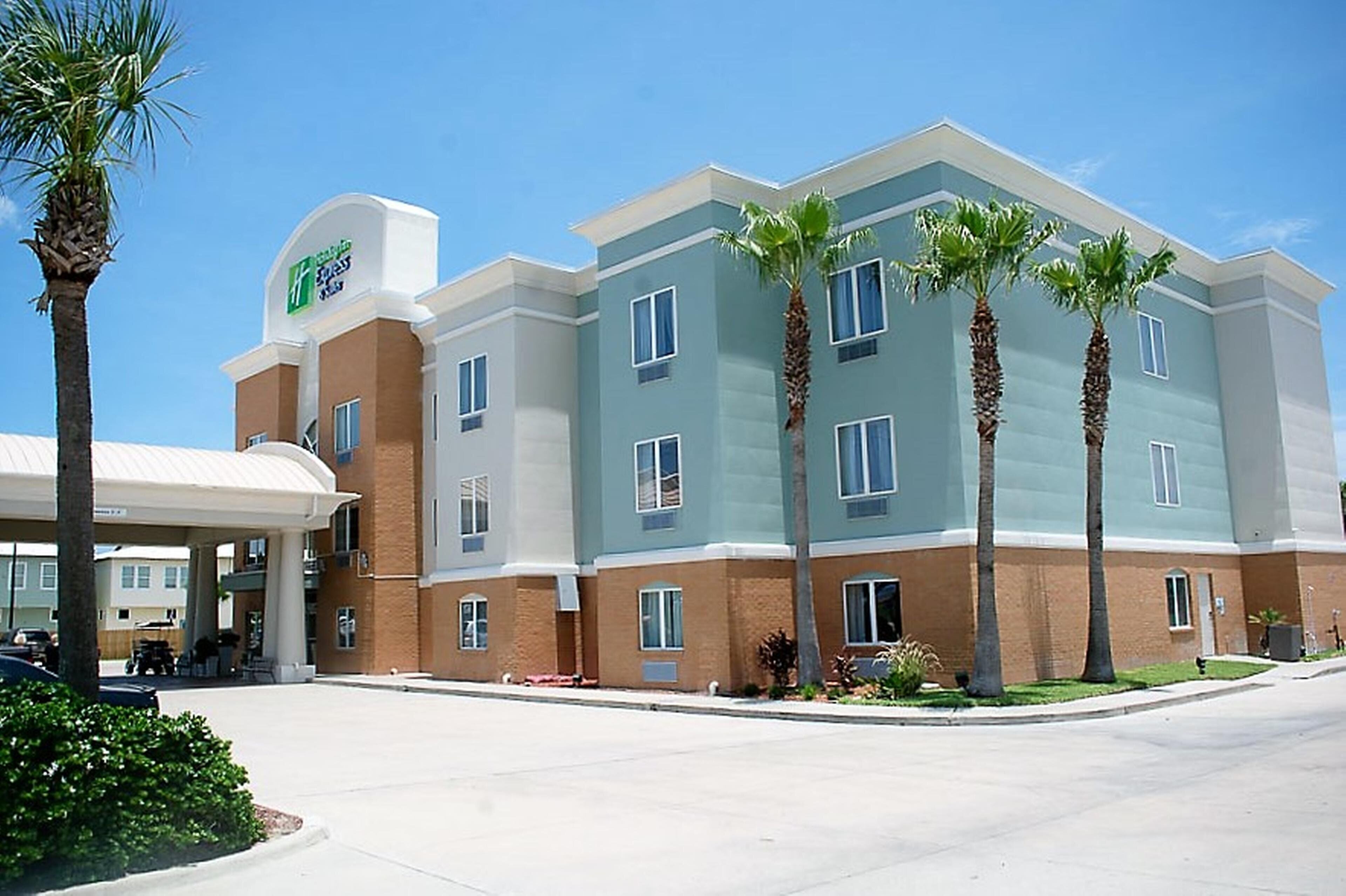 A multi-story hotel with a flat roof, several windows, and a parking area in front.