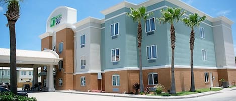 A multi-story hotel with a flat roof, several windows, and a parking area in front.