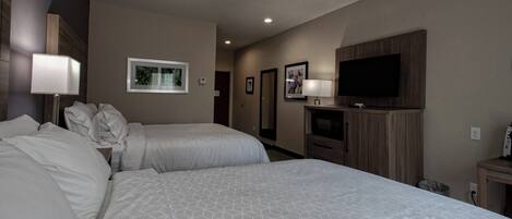 A hotel room with two beds, a TV, a desk, and a mirror.