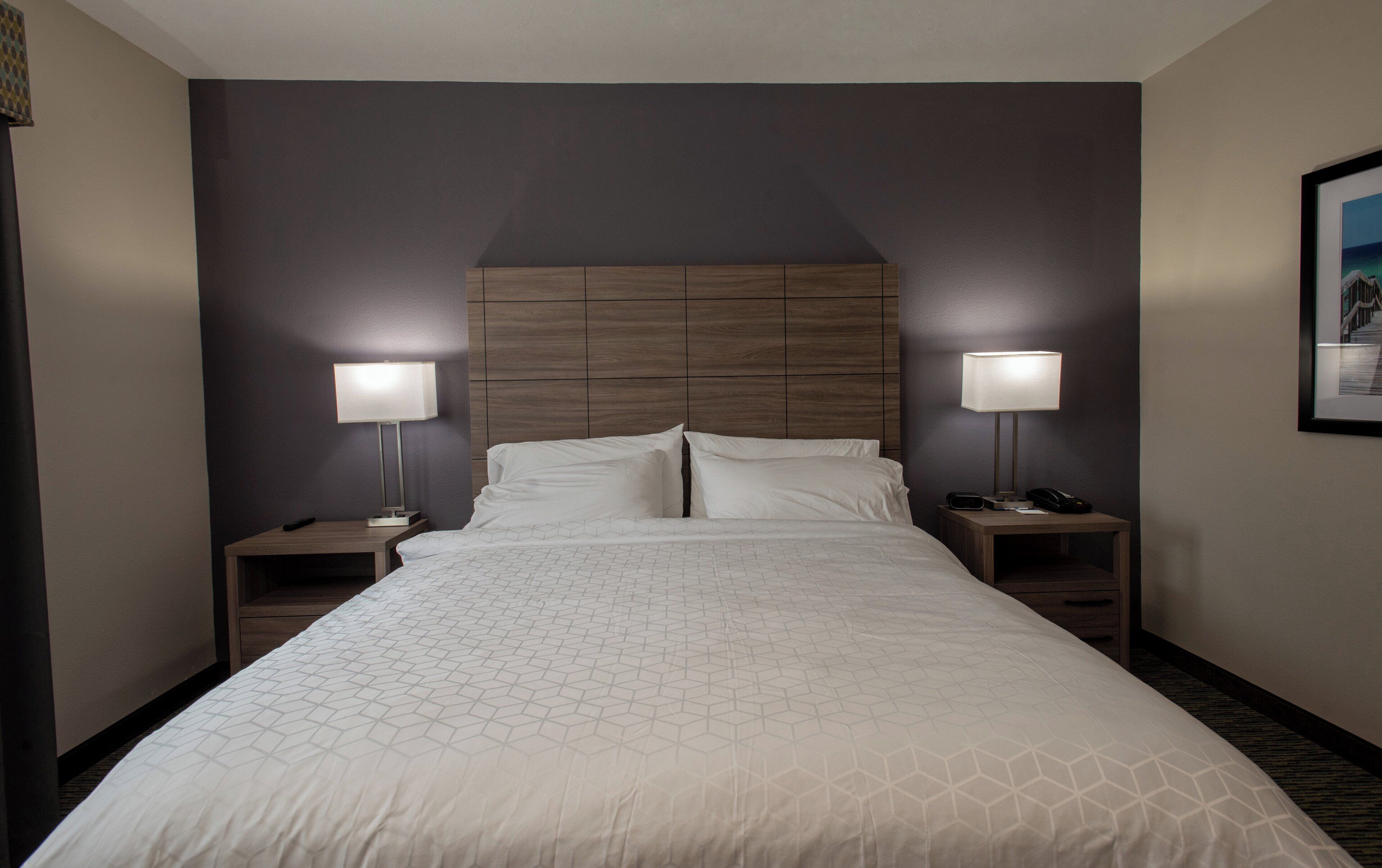 A hotel room with a large bed, two bedside tables, a headboard, and two wall-mounted lamps.
