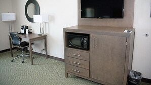 A hotel room with a desk, chair, microwave, TV, and a cabinet.