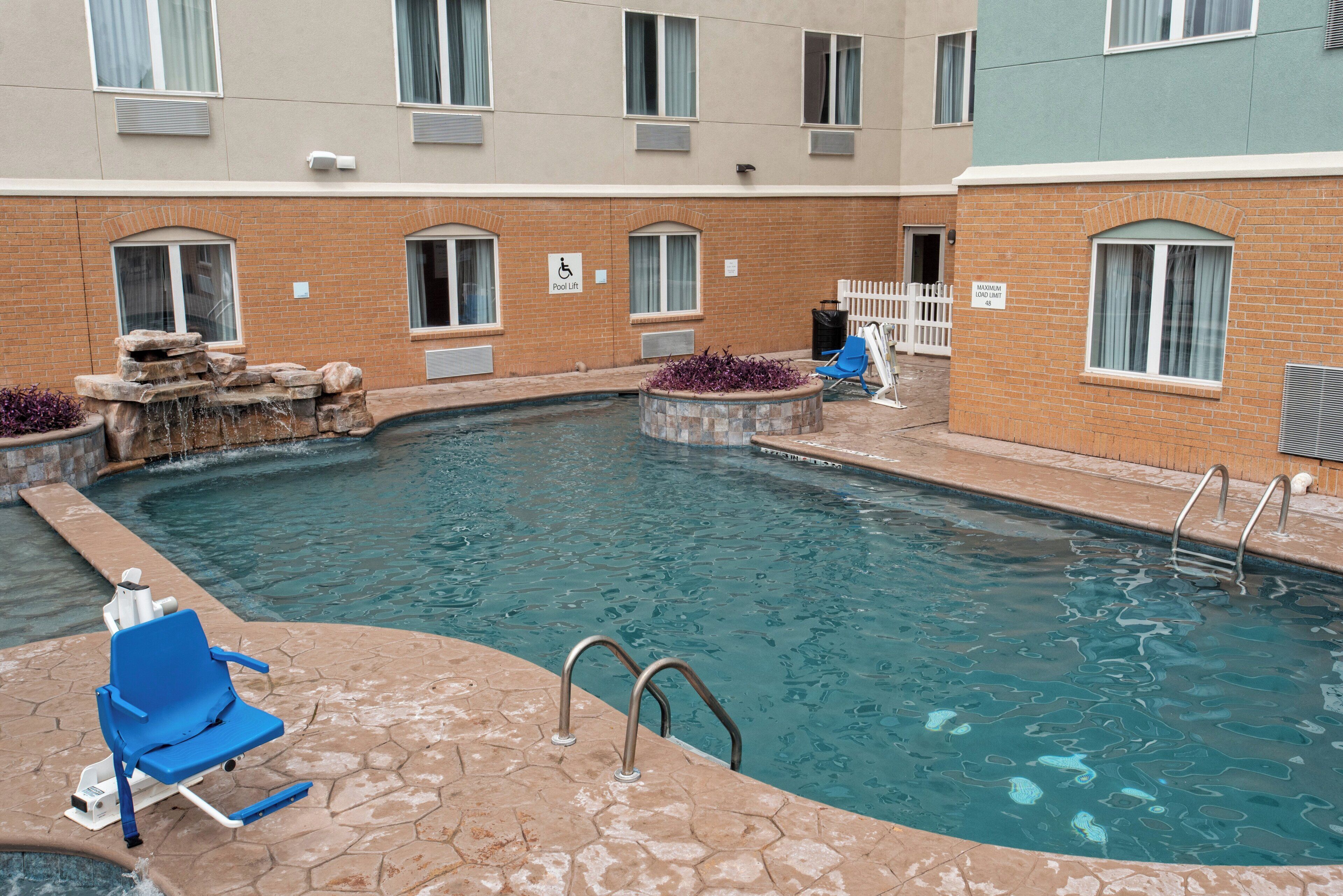 A swimming pool with a pool lift, a blue lounge chair, and a stone waterfall feature.