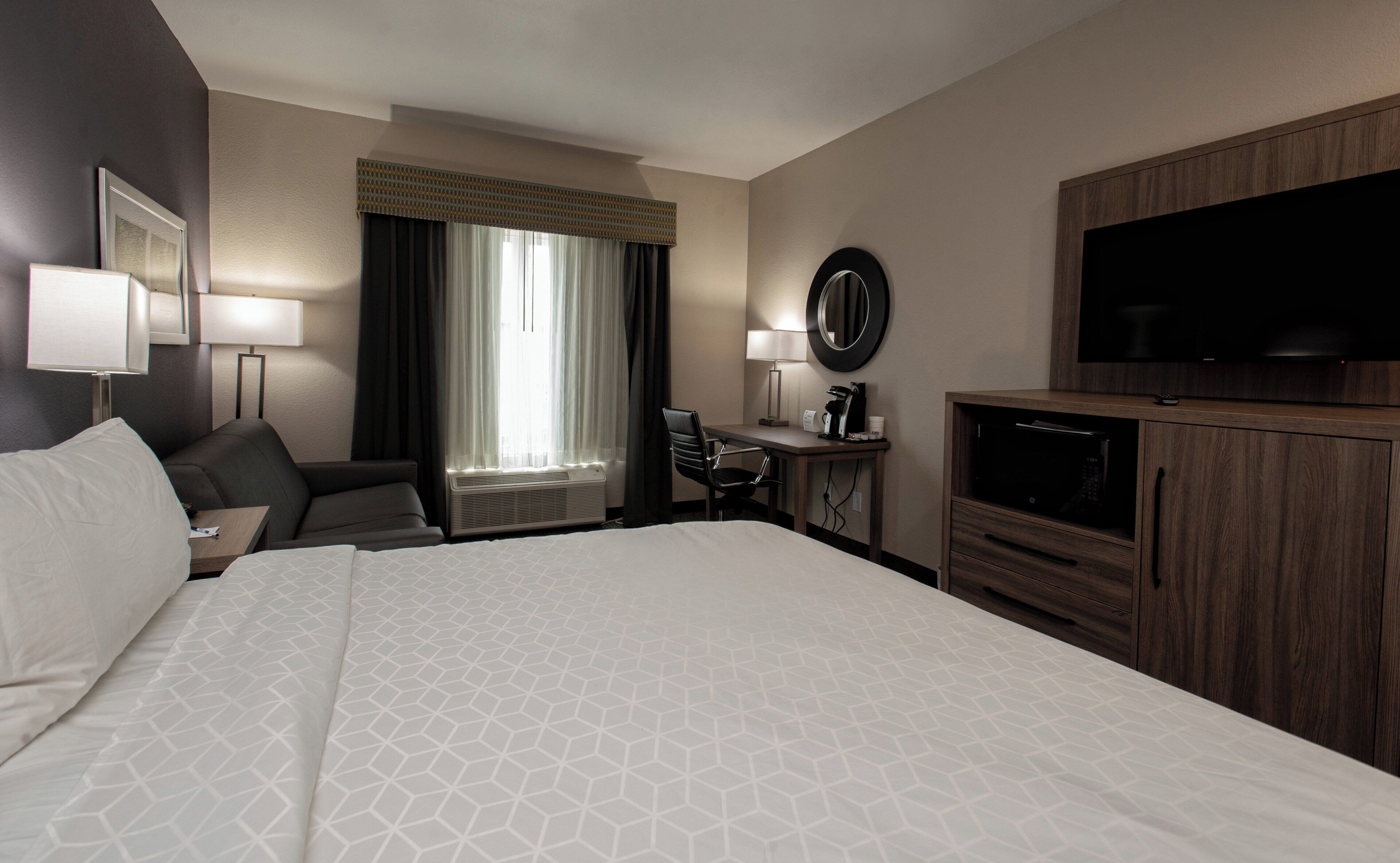 A hotel room with a large bed, a desk with a chair, a television, and a window with curtains.