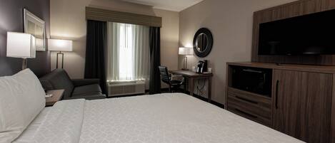 A hotel room with a large bed, a desk with a chair, a television, and a window with curtains.