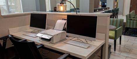 A hotel workspace with two desktop computers, a printer, and a lamp.
