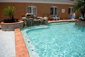 A swimming pool with a waterfall feature, lounge chairs, and a pool lift sign.