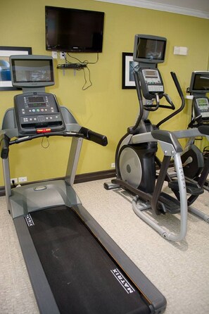 Un gimnasio con cintas de correr, bicicletas estáticas y un televisor montado en la pared.