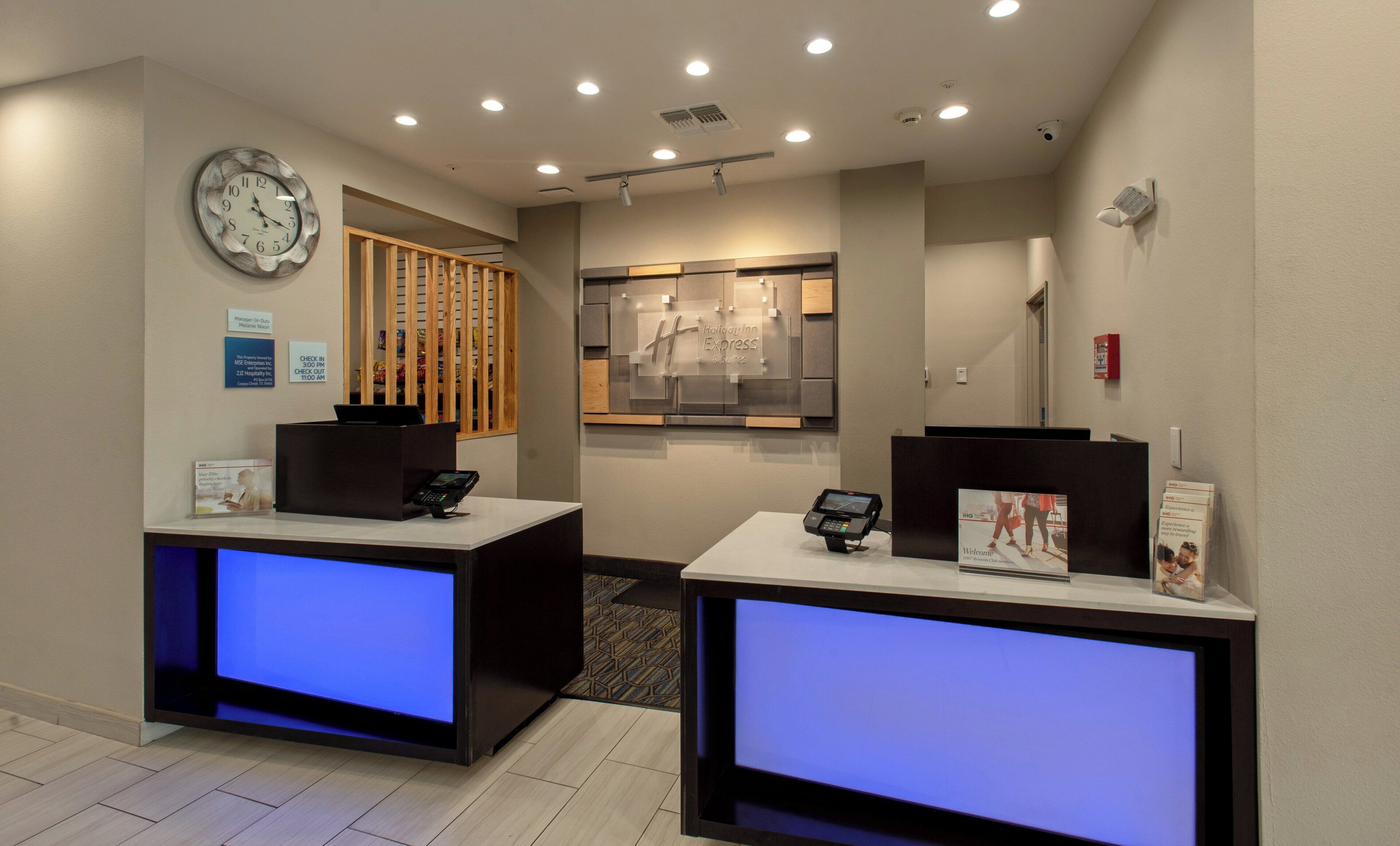 A hotel reception area with two reception desks, a clock, and a sign for the Holiday Inn Express.