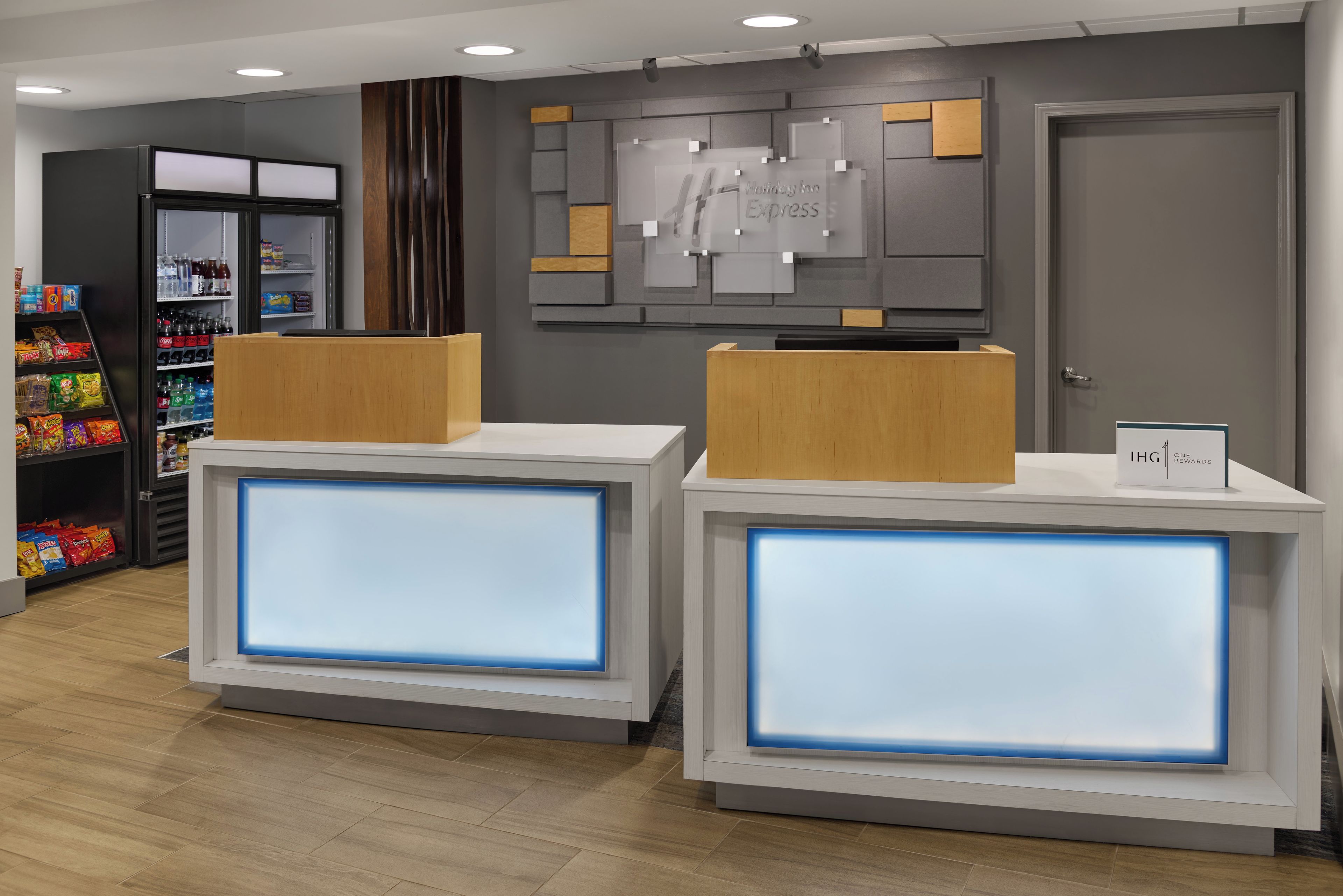 A hotel reception desk with a digital display, a Holiday Inn Express sign, and a Coca-Cola refrigerator.