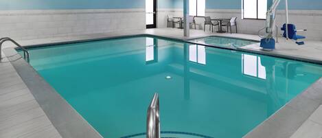 Una piscina con agua azul cristalina, paredes con azulejos y una habitación iluminada por el sol, con una puerta y una ventana.