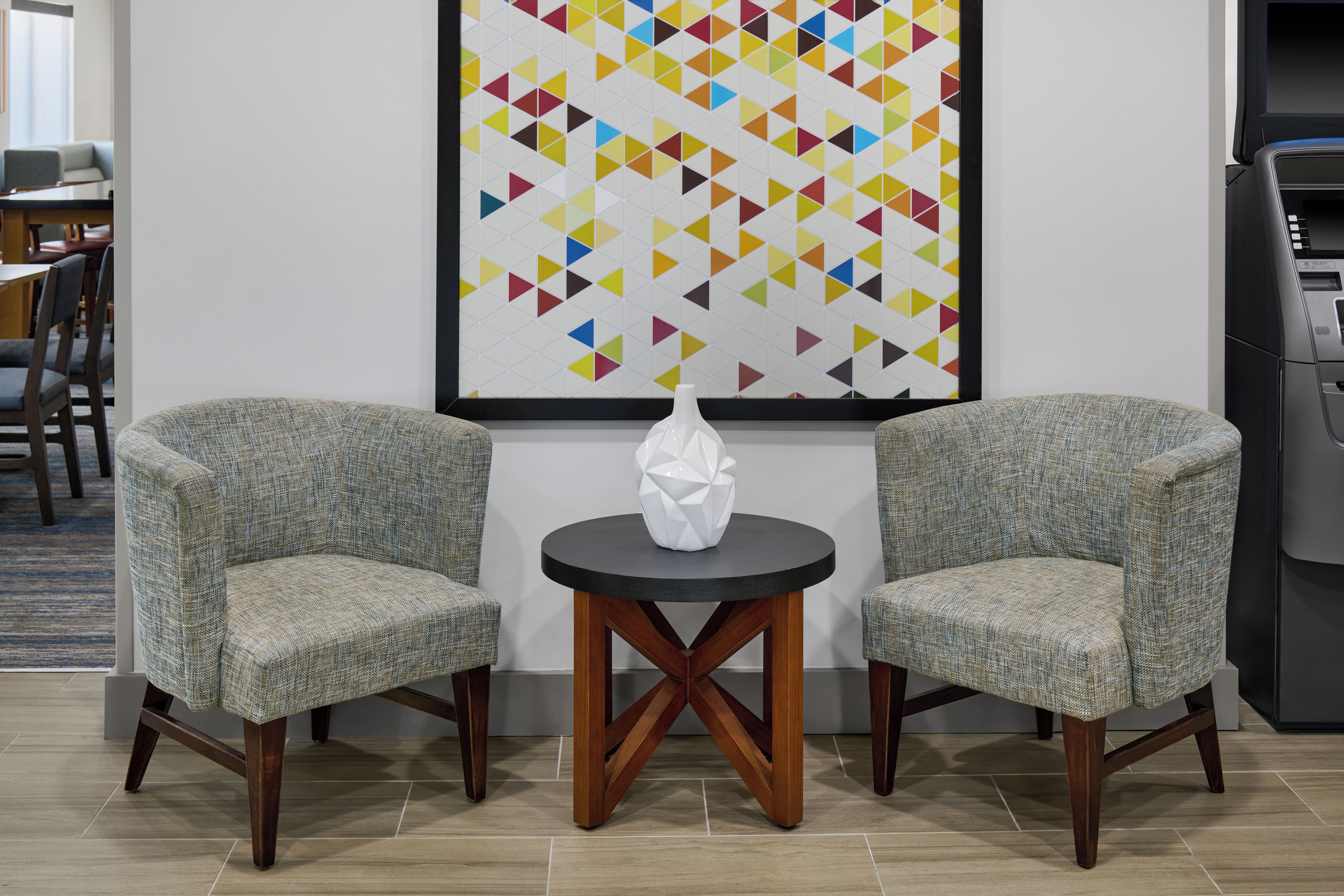 Een kamer met twee fauteuils, een klein rond tafeltje en een kleurrijk kunstwerk met geometrische patronen.