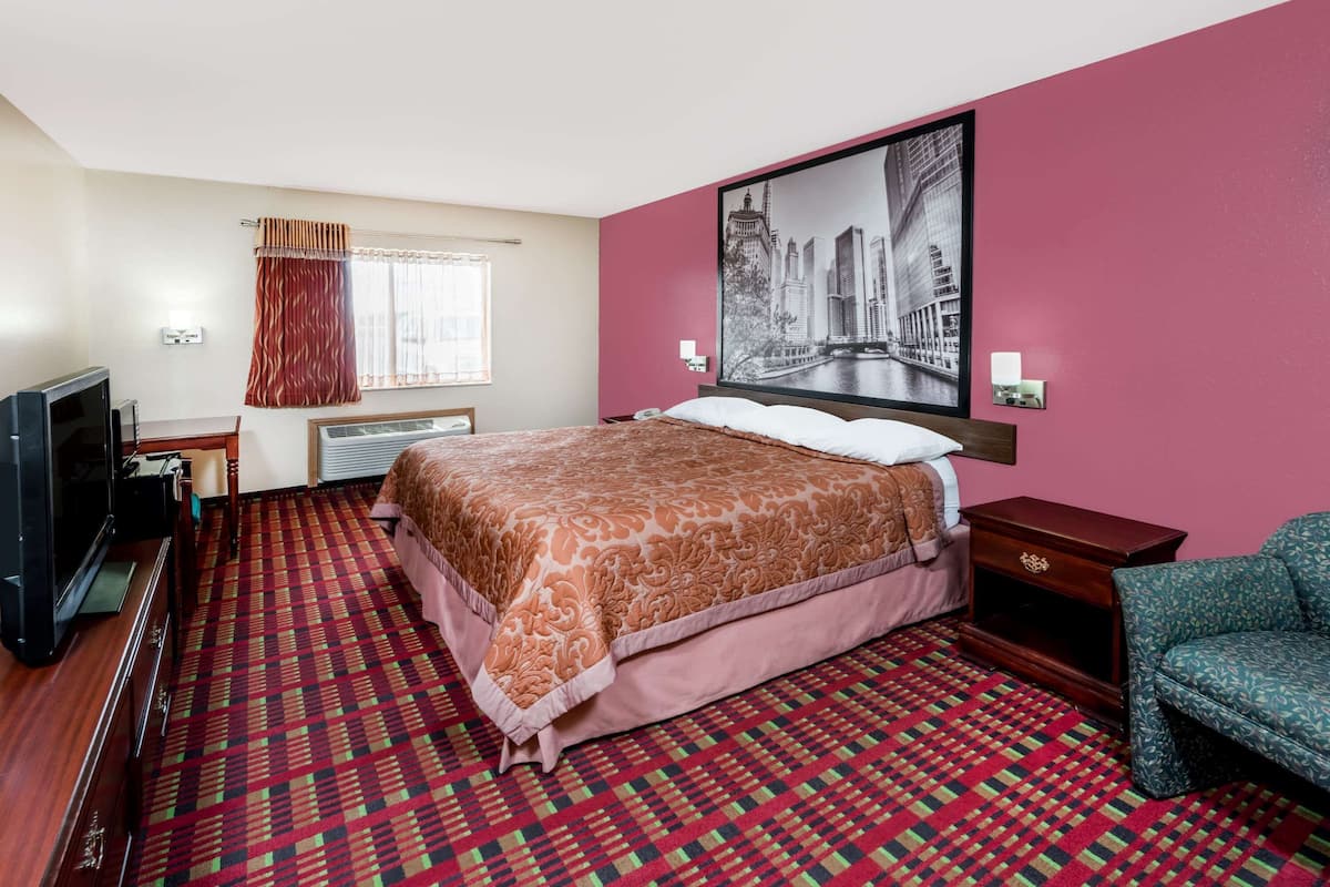 Quarto de hotel com uma cama grande, televisão, escrivaninha e uma cadeira.