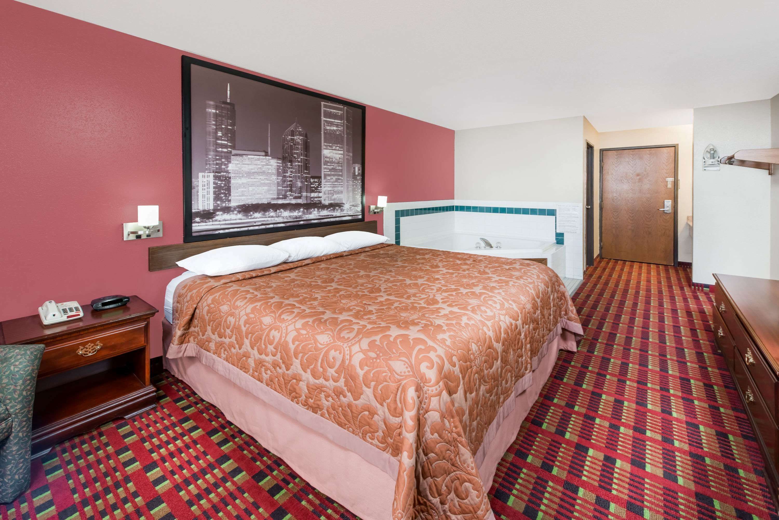 Une chambre d’hôtel avec un grand lit, un tableau représentant un paysage urbain accroché au mur, une salle de bain avec un lavabo blanc et une moquette à motifs.