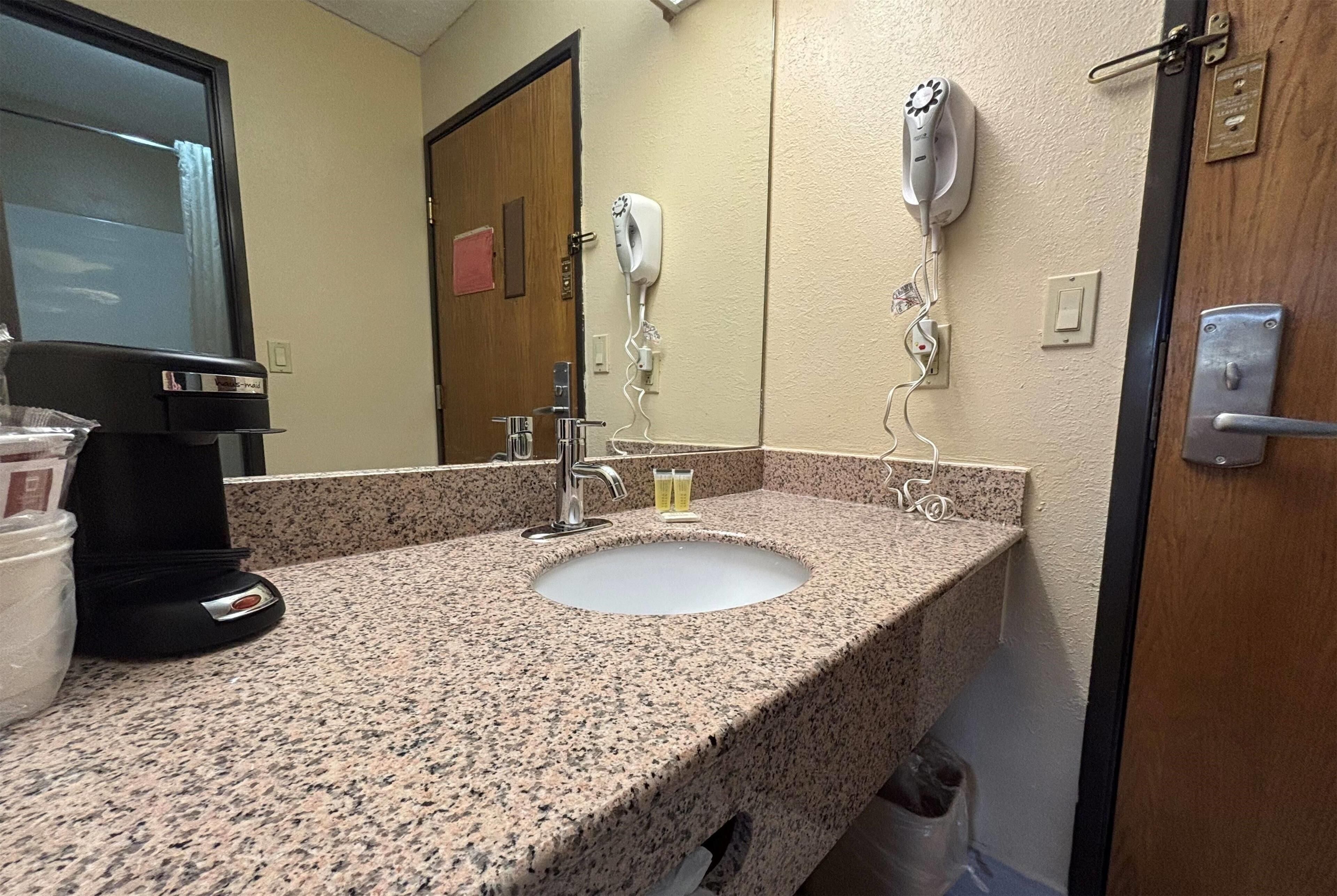 A bathroom with a granite countertop, a sink, a hairdryer, and a mirror.