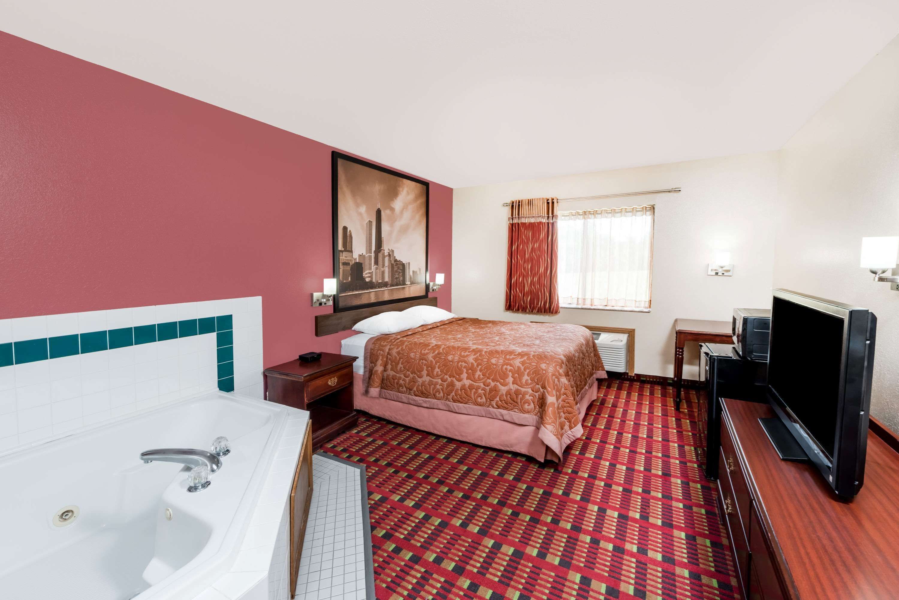 Habitación de hotel con una cama grande, televisión, escritorio, ventana con cortinas y un cuadro en la pared.