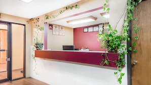 A reception area with a red counter, a computer, framed certificates, and potted plants.