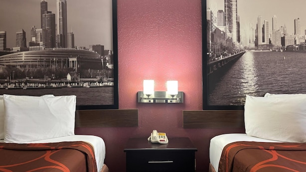 A hotel room with two beds, a nightstand with a phone, and a wall-mounted light fixture.
