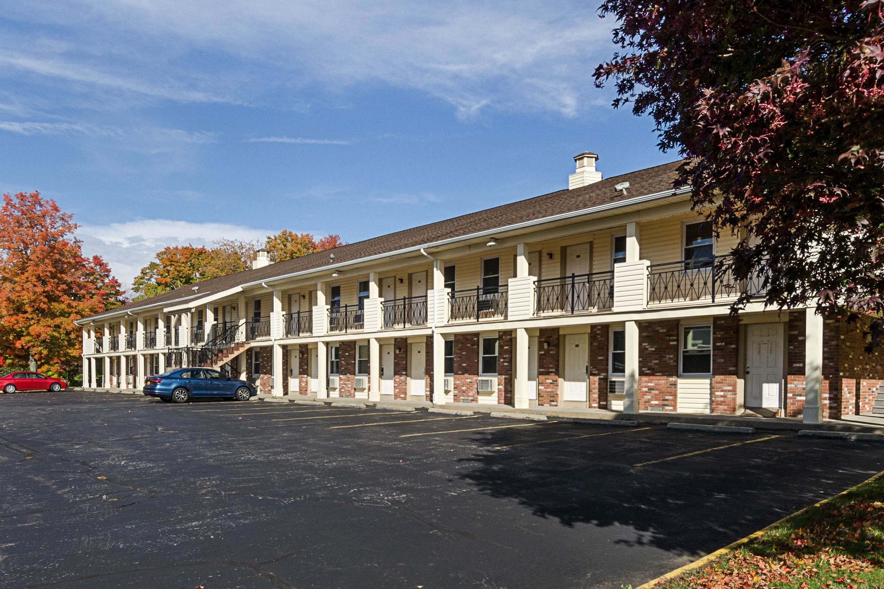 Un motel con una hilera de habitaciones, un estacionamiento y follaje otoñal.