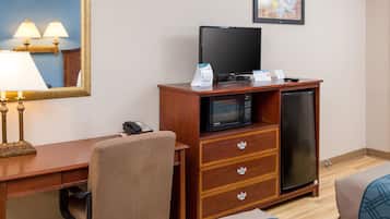 A hotel room with a wooden desk, a chair, a television, a microwave, a refrigerator, and a bed with a patterned cover.