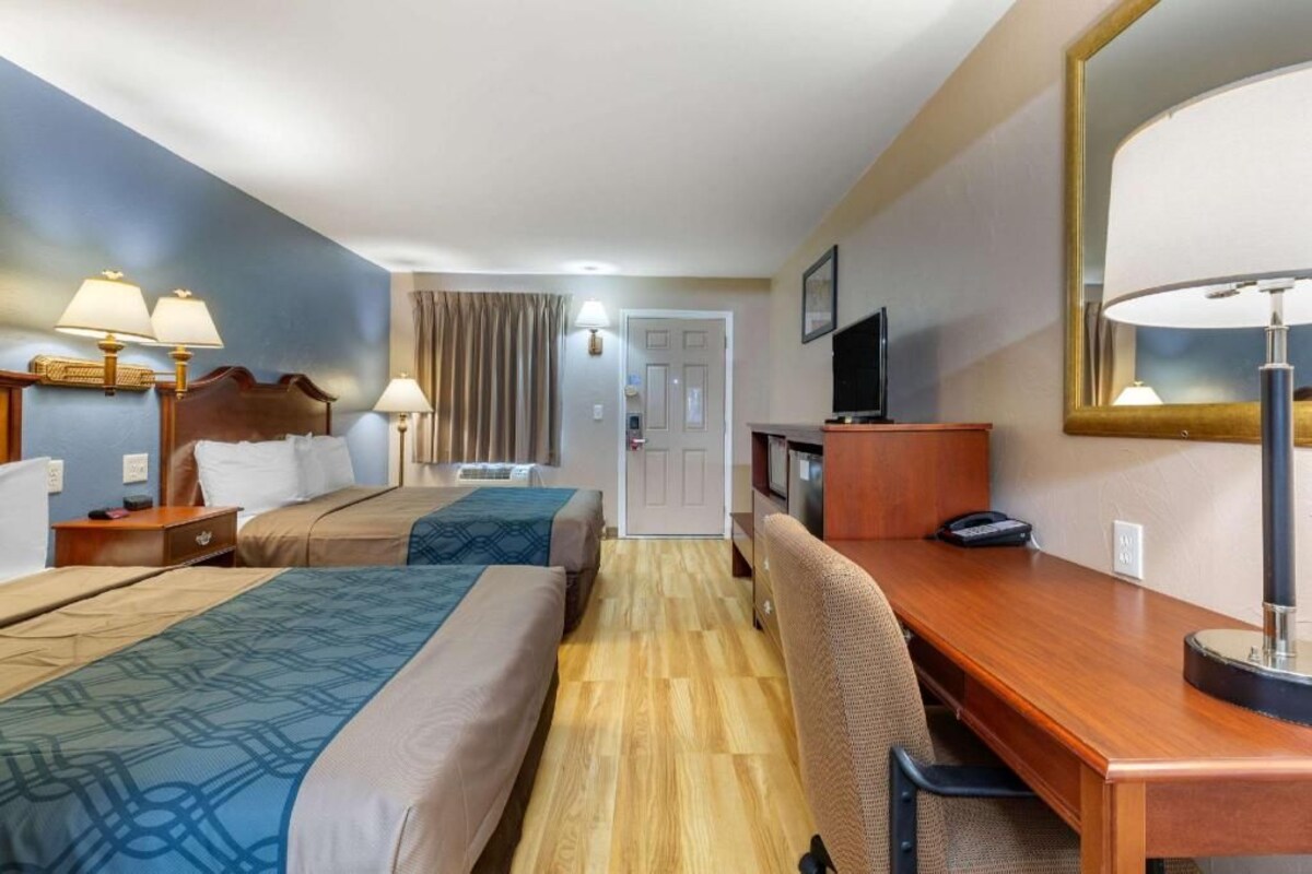 Habitación de hotel con dos camas, un escritorio, una silla, un televisor y un espejo.