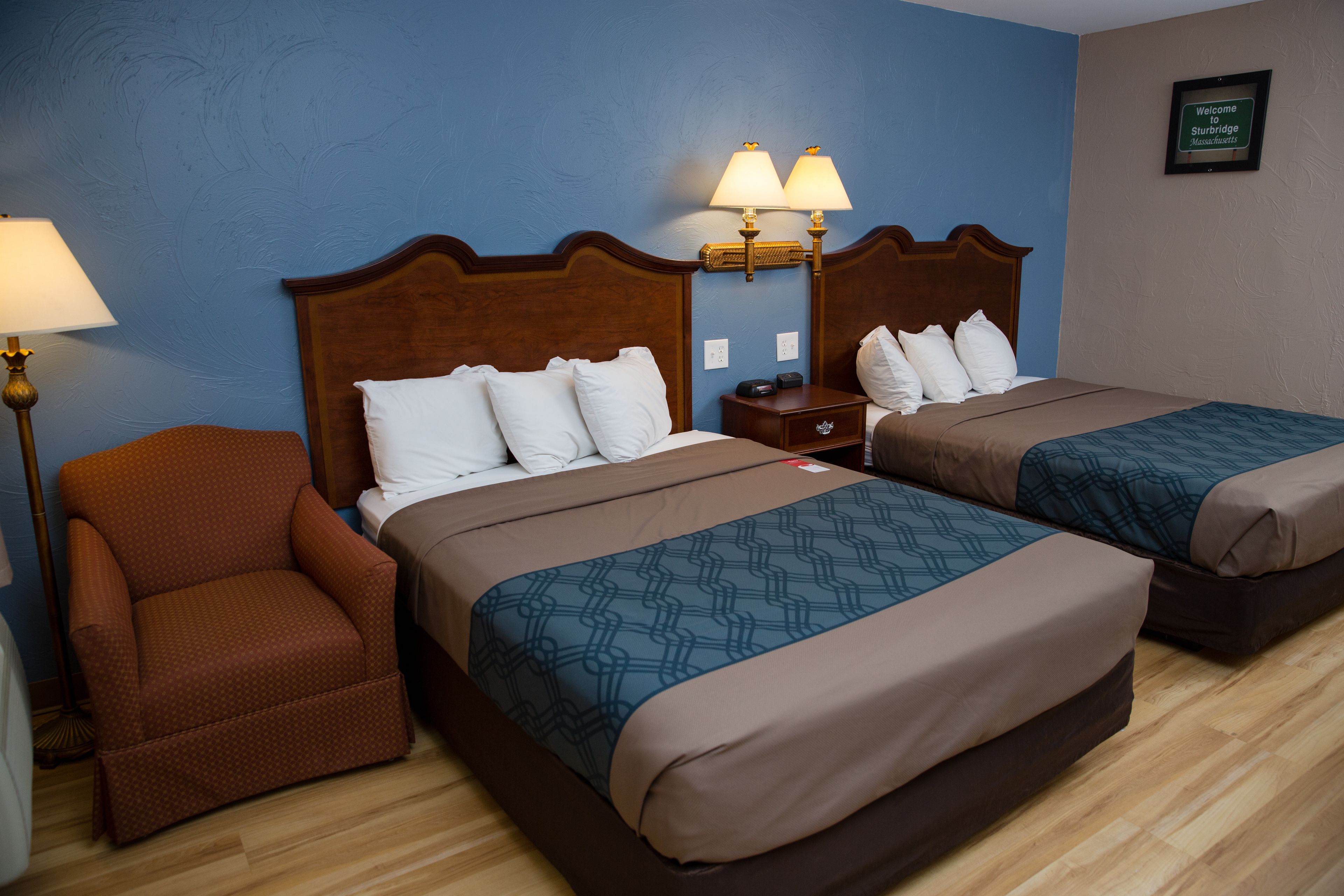 Ein Hotelzimmer mit zwei Betten, einem Nachttisch, einem Sessel und einer Lampe.