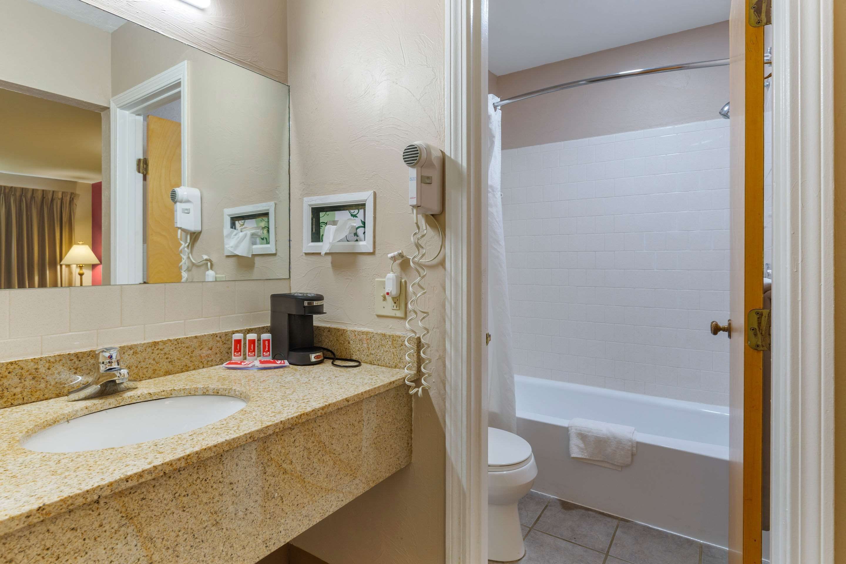 A bathroom with a sink, mirror, hair dryer, and a shower area.