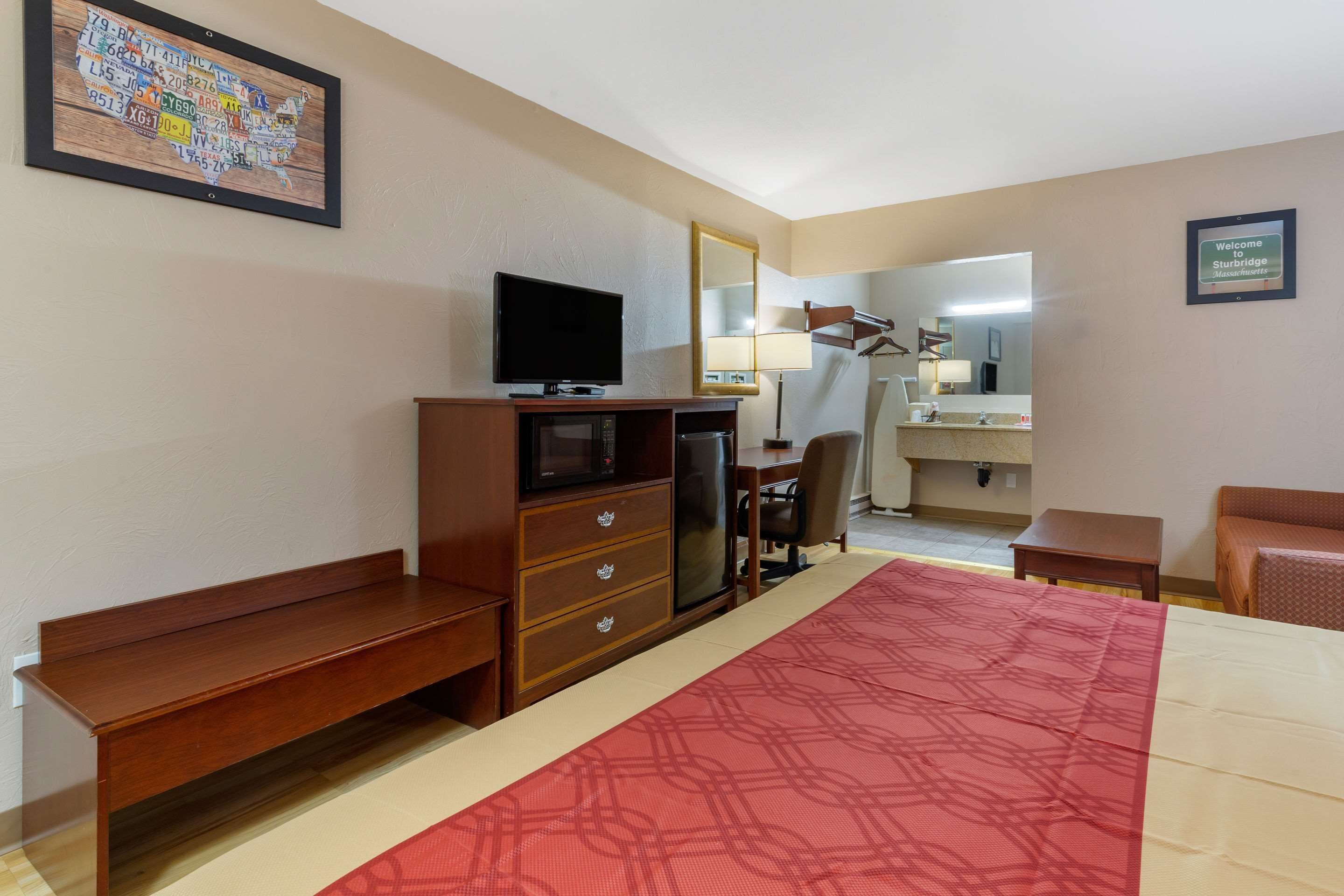 Ein Hotelzimmer mit Bett, Schreibtisch, Fernseher, Mikrowelle, Stuhl und kleinem Tisch.