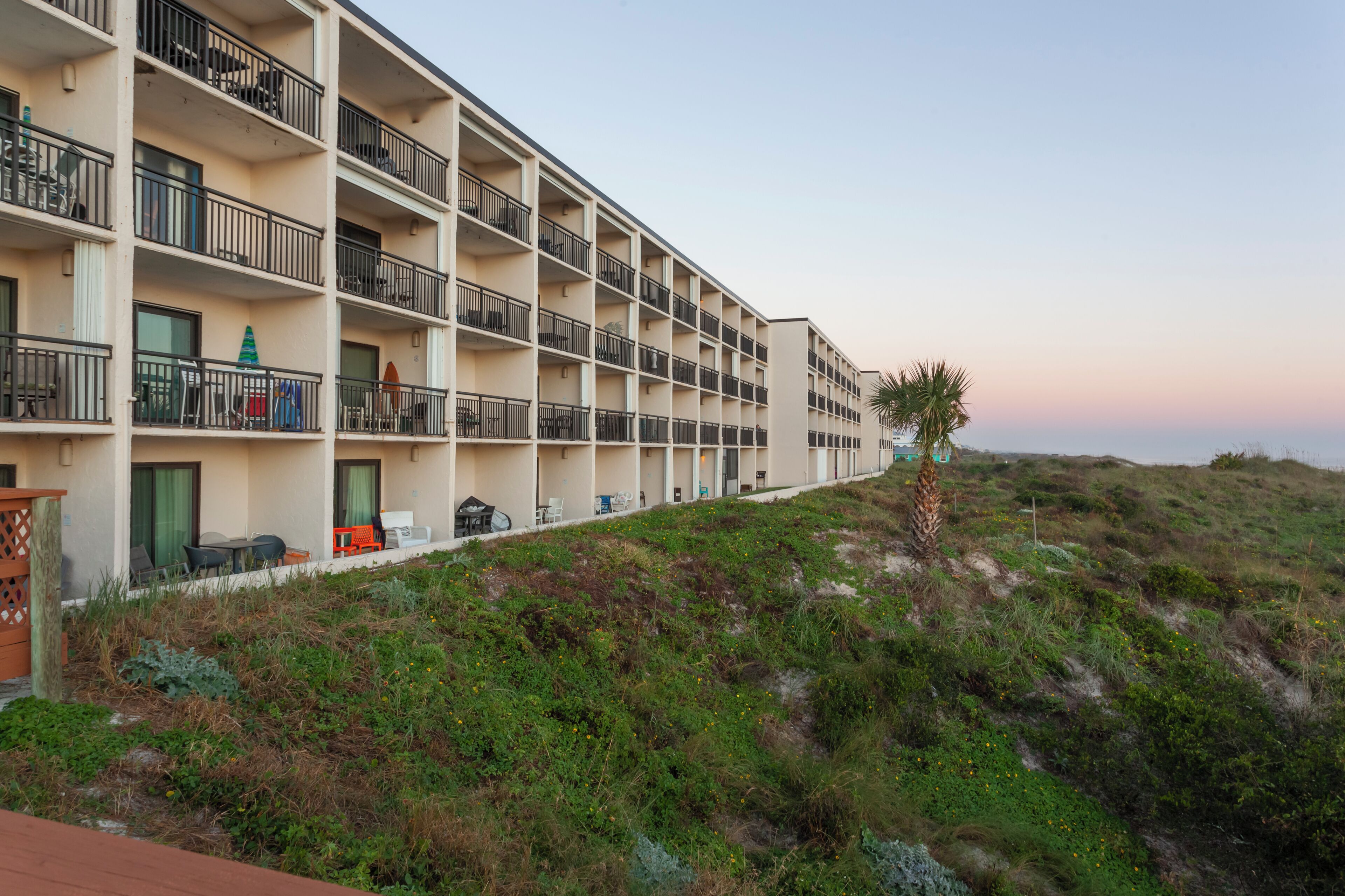 A multi-story hotel with balconies, outdoor seating, and a view of the beach.