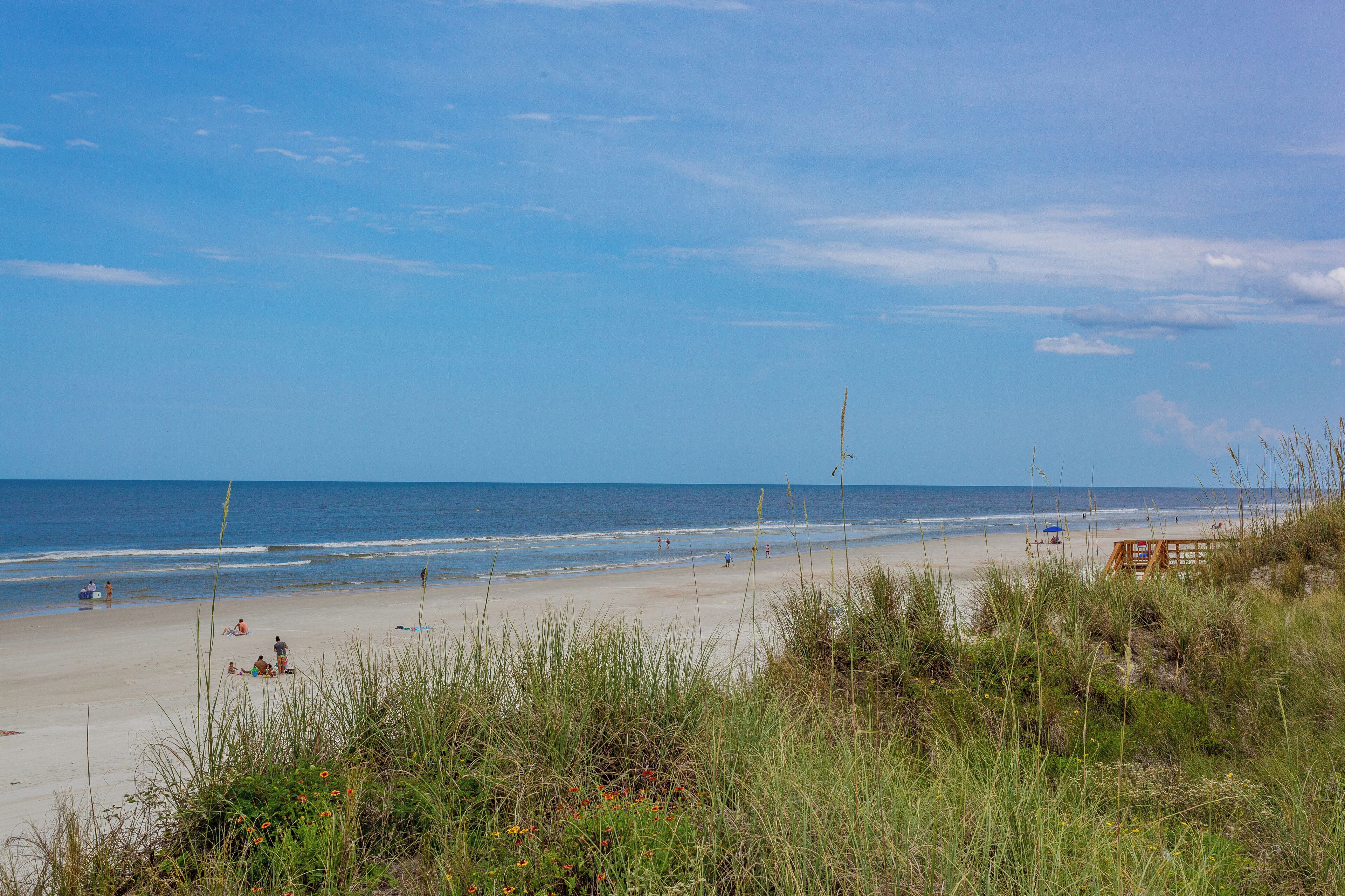 A beach with a wooden boardwalk, grassy dunes, and the ocean in the background.