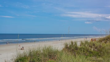 A beach with a wooden boardwalk, grassy dunes, and the ocean in the background.