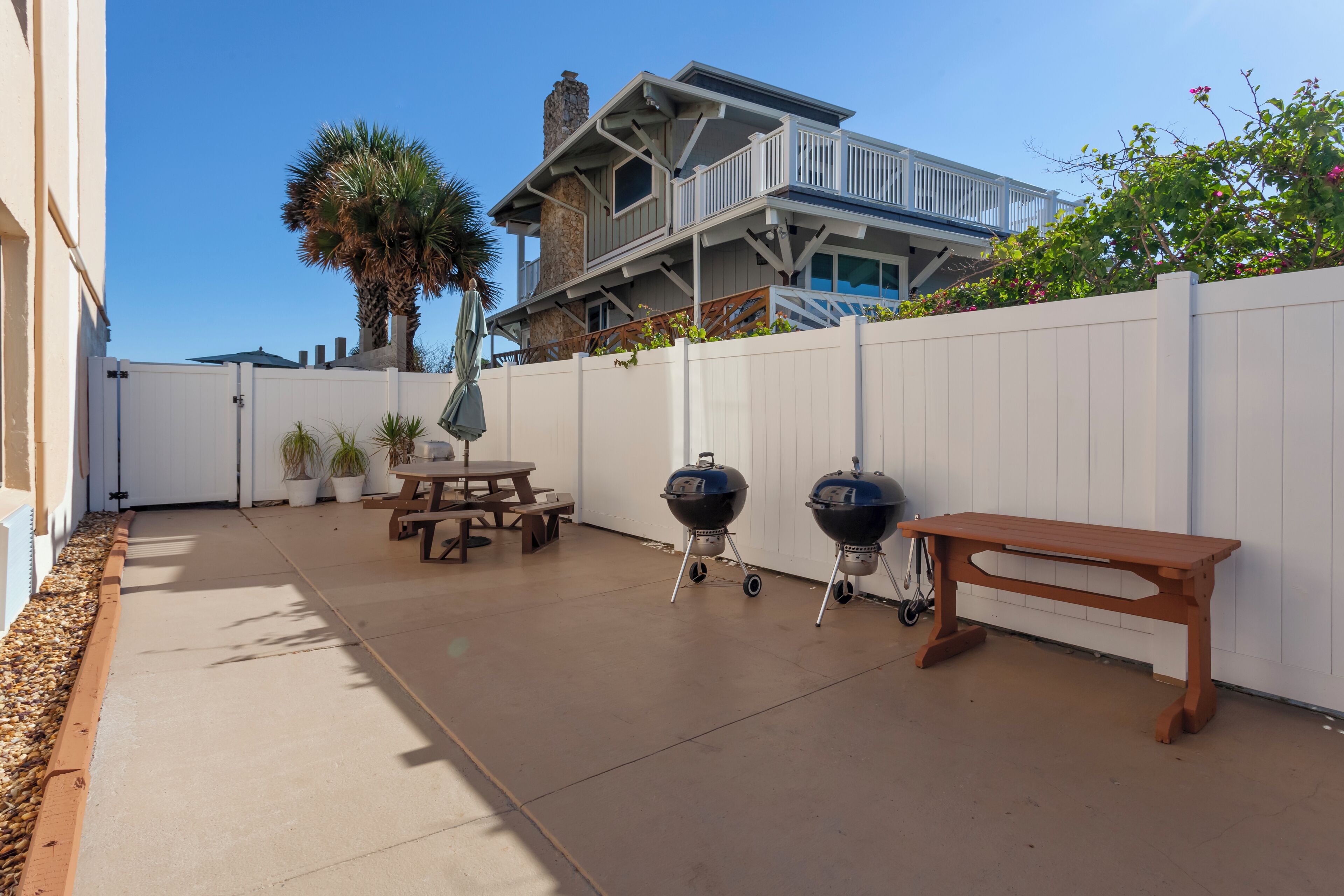 A patio with a concrete floor, two barbecue grills, a wooden bench, and a picnic table.