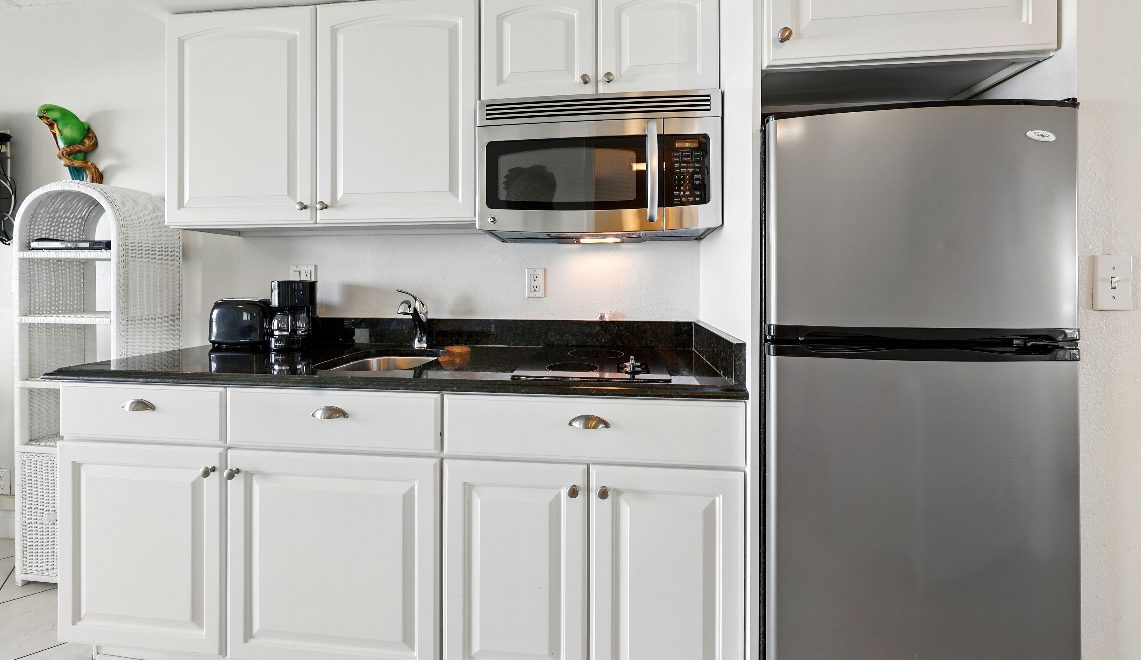 A modern kitchen with white cabinetry, a stainless steel refrigerator, a built-in microwave, and a black countertop.