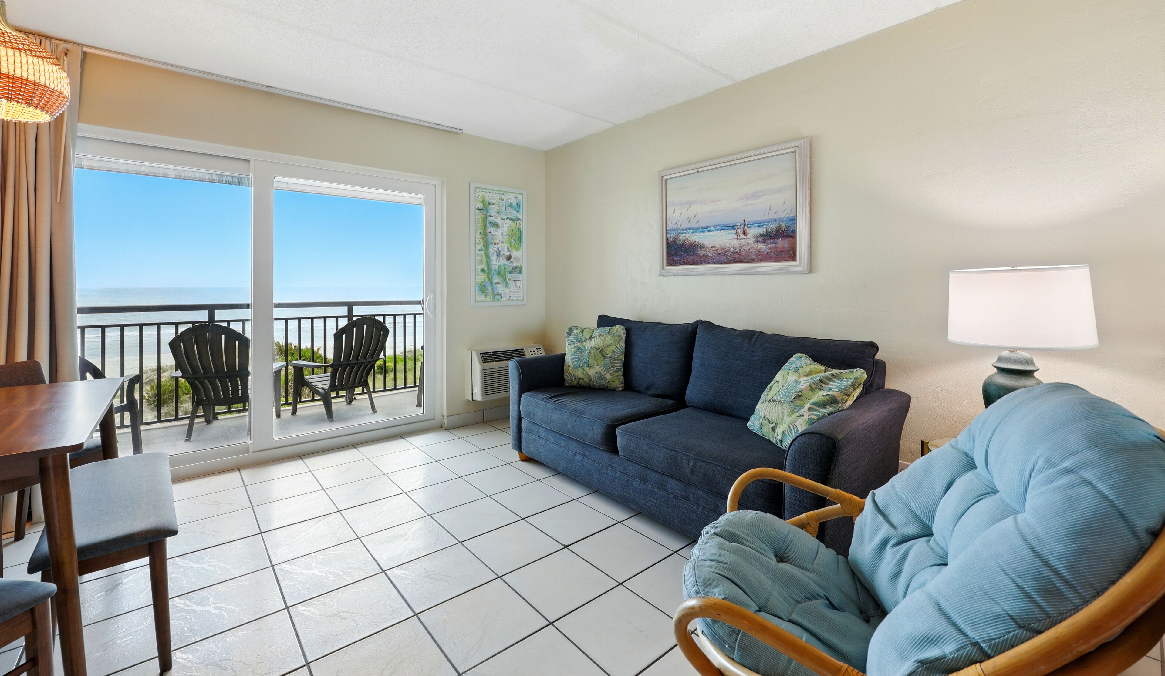 Een woonkamer met balkon en uitzicht op de oceaan, een bank, een stoel en een tafel.