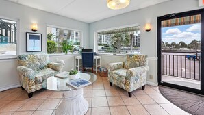 A spacious living area with two patterned armchairs, a glass coffee table, and a laptop on a desk. Large windows offer views of the outside. - Beacher's Lodge Oceanfront Suites (St. Augustine)
