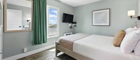 A bedroom with a bed, a television, a framed picture, and a window with curtains.
