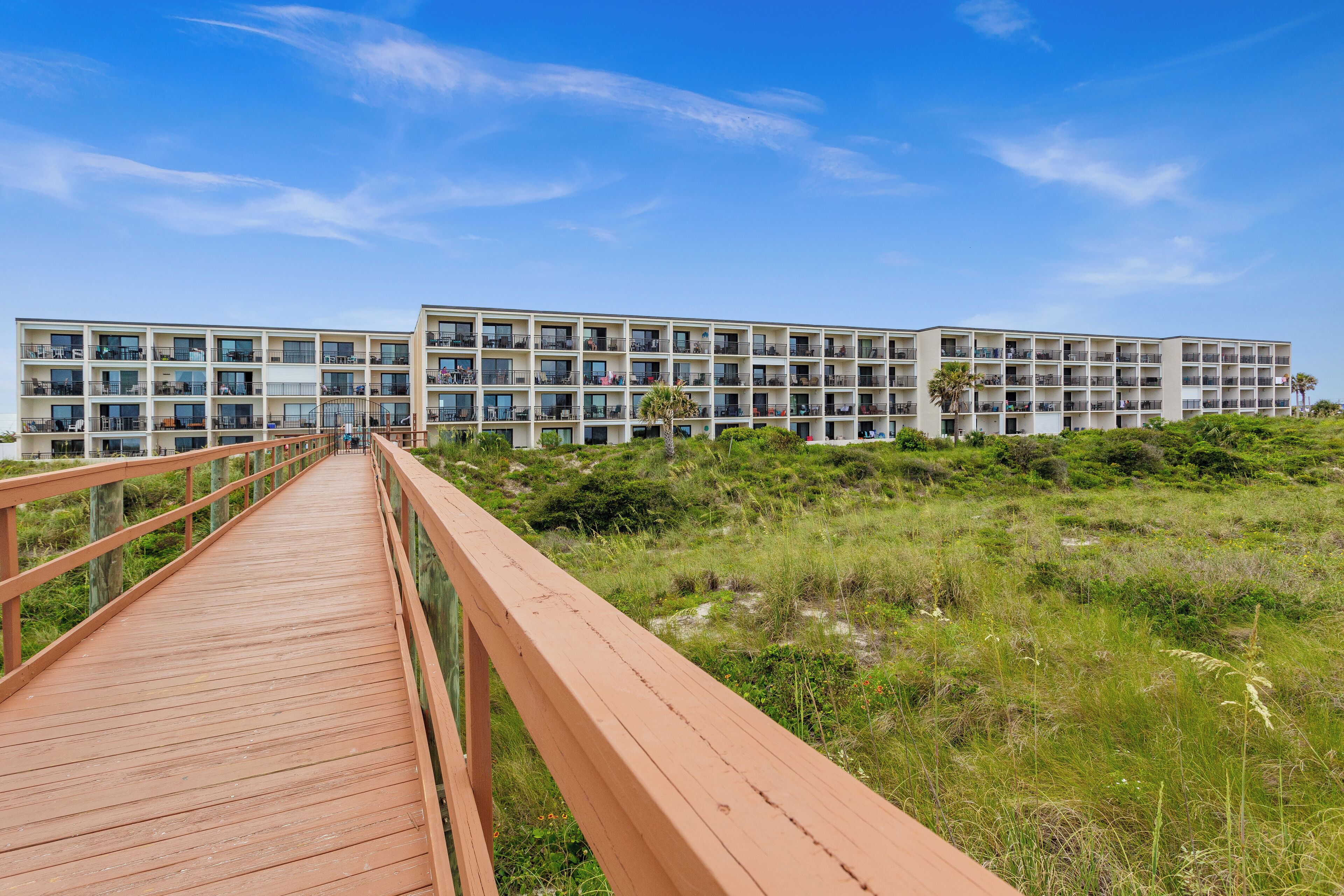 A modern hotel with multiple floors, a wooden walkway, and a natural landscape.