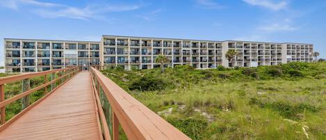 A modern hotel with multiple floors, a wooden walkway, and a natural landscape.